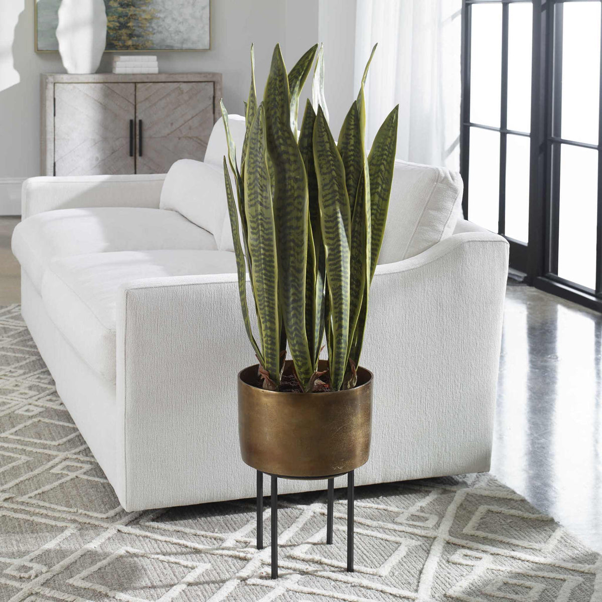 Fasita Planter with life-like snake plant in antique brass pot and matte black metal stand in modern living room.