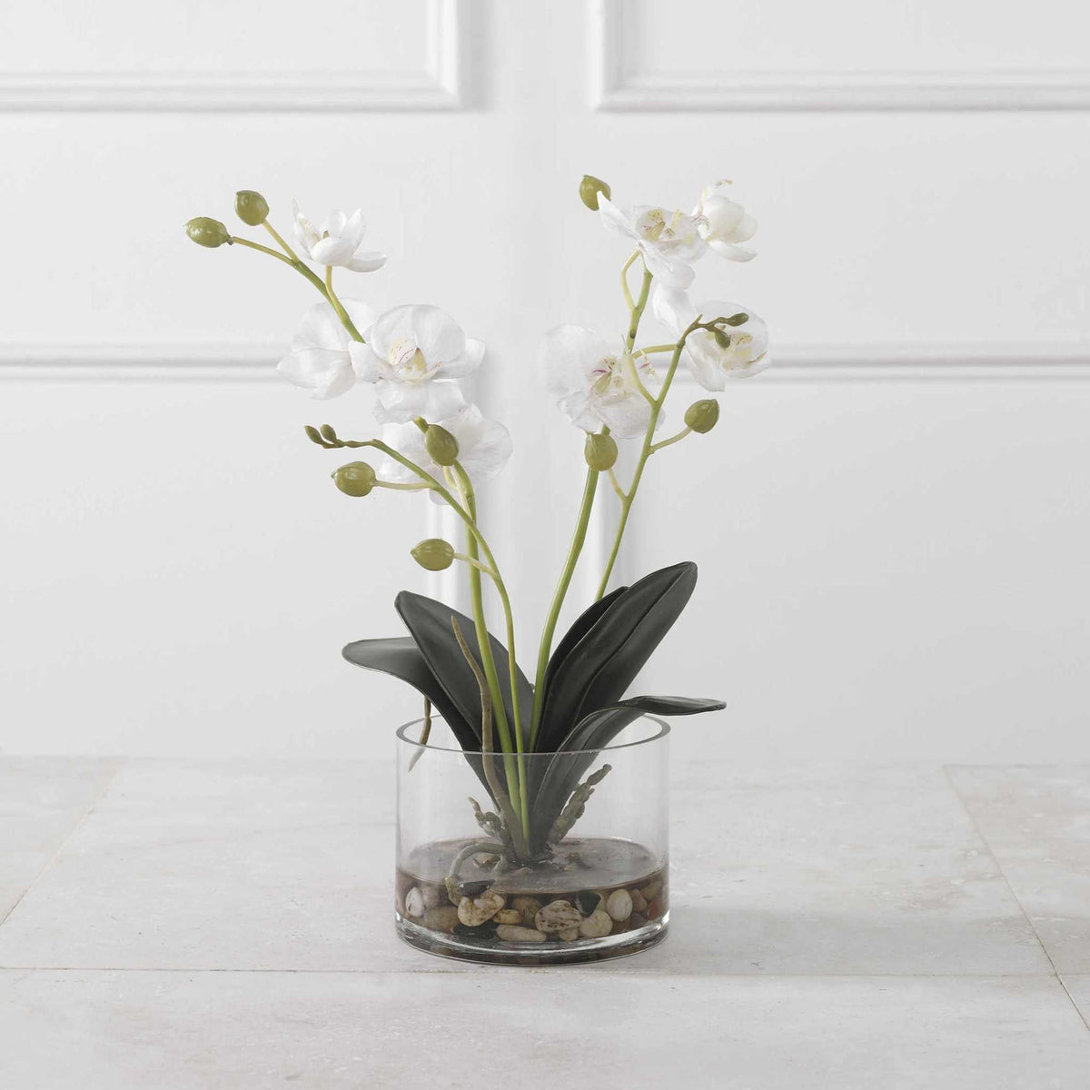 White Glory Orchid in a glass container with faux water and river stones, enhancing room elegance.