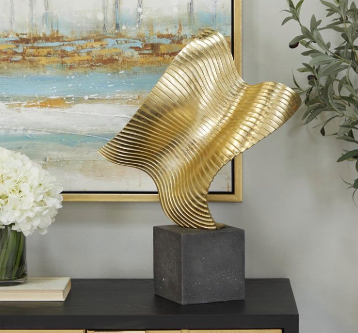 Golden wave sculpture with black stone base in room setting